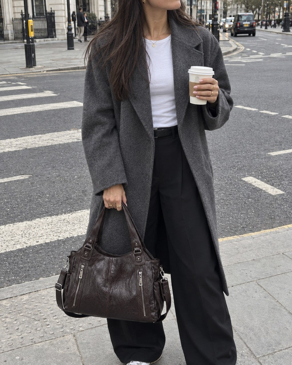 A woman crossing a city street in a long gray coat, coffee in hand, carrying the Soho Tote in brown